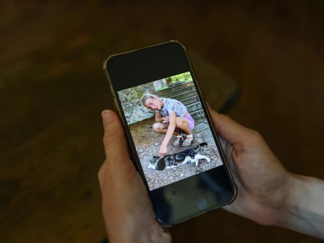Irene Roggero Ugues holding a mobile phone displaying her daughter Rossella's photograph, symbolizing the tragic human cost of social media algorithms